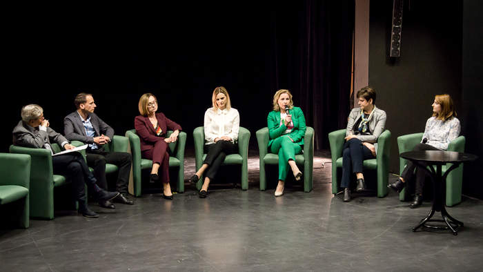 Pokaż zdjęcie: Na scenie w lekkim półokręgu stoi 8 krzeseł. Trwa panel dyskusyjny. 