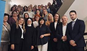 Grupowe zdjęcie uczestników konferencji. Kilkanaście osób stoi na schodach i przed nimi, pozując wspólnie do fotografii. W pierwszym planie znajdują się przedstawiciele organizatorów i uczestnicy spotkania.