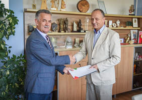 Dwóch mężczyzn, stoją, ściskają sobie dłonie, przekazują dokumenty