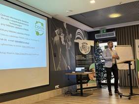 Pokaż zdjęcie: Prelekcję wygłasza wysoki mężczyzna, w tle ekran z logo CIDON.