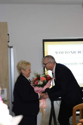 Pokaż zdjęcie: Mężczyzna w garniturze wręczający kobiecie bukiet kwiatów.)