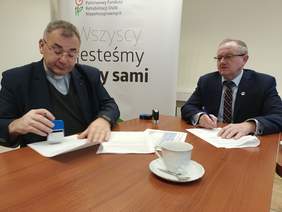 Pokaż zdjęcie: Dyrektor Oddziału Świętokrzyskiego PFRON Andrzej Michalski podpisuje aneks z ks. Bogusławem Pituchą dyrektorem Sandomierskiej Caritas