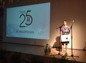 Pokaż zdjęcie: Na scenie przedstawiciel Oddziału Małopolskiego PFRON - Bogusława Słońska podczas przekazywania gratulacji i życzeń. W tle napis "25 lat"