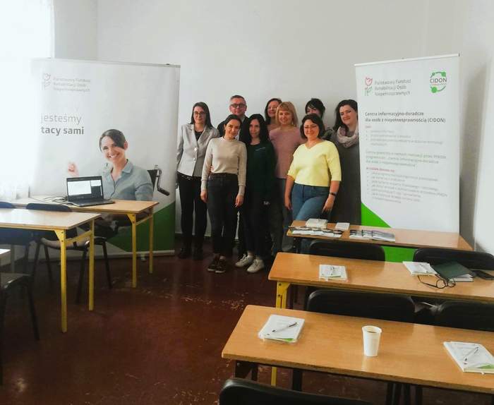 Zdjecie grupowe uczestników i prelegentów, po bokach stoją banery z logo i promocją PFRON-u