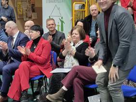 Na krzesłach siedzą zaproszeni goście i biją brawo.