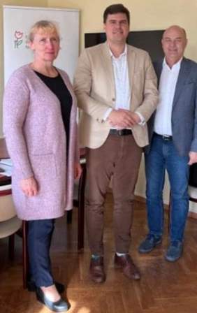 Pokaż zdjęcie: Od lewej kobieta, i dwóch mężczyzn, stoją i uśmiechają się. Za nimi baner PFRON