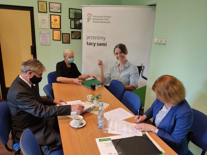 Pokaż zdjęcie: Przy stole siedzi mężczyzna i dwie kobiety, podpisują umowy rozłożone na stole