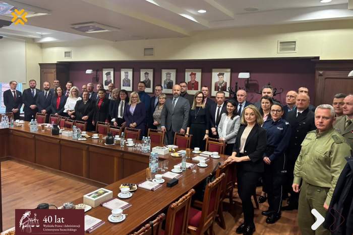 Pokaż zdjęcie: Zdjęcie grupowe uczestników pierwszego posiedzenia Rady Interesariuszy Wydziału Prawa i Administracji Uniwersytetu Szczecińskiego. Ponad trzydzieści osób – przedstawicieli nauki, administracji oraz służb mundurowych (widoczni funkcjonariusze Policji, Wojska Polskiego i Straży Granicznej) – pozuje w eleganckiej sali konferencyjnej. Uczestnicy stoją za długim, drewnianym stołem zastawionym filiżankami i wodą. W tle na bordowej ścianie widać poczet portretów rektorskich. W lewym dolnym rogu znajduje się logotyp obchodów 40-lecia Wydziału.