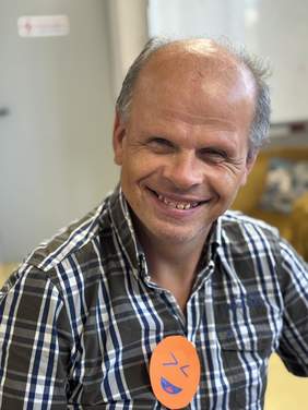 Pokaż zdjęcie: Uśmiechnięty mężczyzna w koszuli na której ma pomarańczową wpinkę