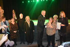 Pokaż zdjęcie: Grupa elegancko ubranych osób stoi podczas uroczystości. Jedna z nich wręcza tegorocznej laureatce statuetkę „Solnego Kosa”