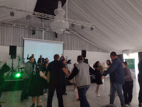 Osoby przed sceną tańczą, trzymają sie za ręce w kole