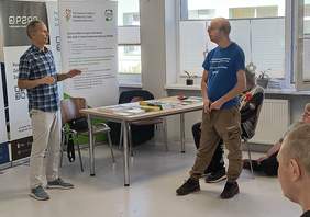 Pokaż zdjęcie: Uczestnicy spotkania przed biurkiem PFRON