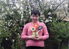 Pokaż zdjęcie: Uczestniczka zajęć pozuje z wykonanymi ręcznie kwiatami, w tle drzewa