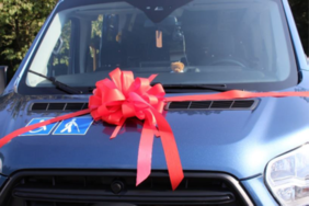 Pokaż zdjęcie: Zbliżenie na maskę granatowego autobusu przystrojonego kokardą.