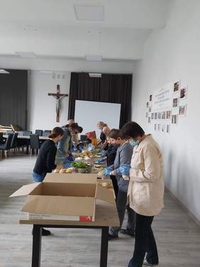 w dużej sali grupa osób, stojących po obu stronach stołu przygotowuje kanapki