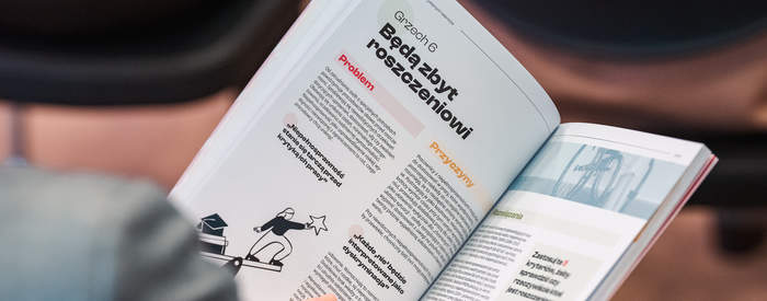 Pokaż zdjęcie: Zbliżenie dłoni trzymającej otwartą książkę z artykułem o niepełnosprawności, kadr wózka inwalidzkiego, tekst w języku polskim.