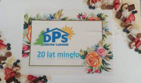 Pokaż zdjęcie: Tort w kształcie prostokąta udekorowany kwiatami z napisem DPS 20 lat minęło.