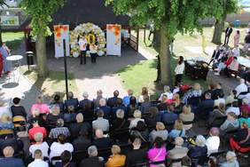 Pokaż zdjęcie: Kilkadziesiąt osób siedzi na krzesełkach i przygląda się kobiecie i mężczyźnie z mikrofonem, za nimi łuk z balonów