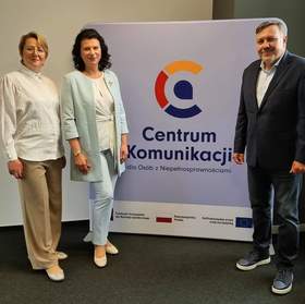 Dwie kobiety i jeden mężczyzna elegancko ubrani stoją przy rollupie z napisem i logo Centrum Komunikacji.