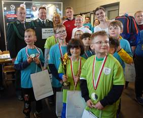 Pokaż zdjęcie: Tłum dzieci i dorosłych. Na pierwszym planie uśmiechnięte dzieci, trzymają puchary i torebki z logo PFRON, na szyjach mają medale.