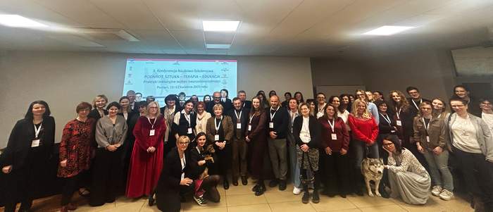 Pokaż zdjęcie: Grupa około 50 osób stoi w sali konferencyjnej na tle dużego ekranu. Na ekranie wyświetlany jest slajd promujący III Konferencję Naukowo-Szkoleniową „Podmiot. Sztuka – terapia – edukacja. Praktyki inkluzyjne wobec neuroróżnorodności”.