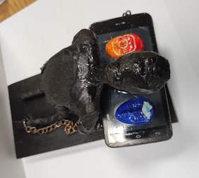 Pokaż zdjęcie: Zdjęcie rzeźby w kolorze czarnym przedstawiająca człowieka klęczącego nad telefonem i przykutego do niego łańcuchami. Na telefonie są trzy twarze z logo facebook, instagram i twitter