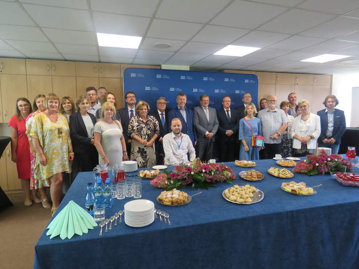 Zdjęcie grupowe wszystkich uczestników otwarcia punktu Cidon w Bydgoszczy, na pierwszym planie stół z kwiatami i przekąskami