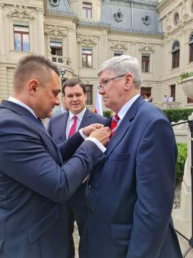 Pokaż zdjęcie: wręczenie odznaki przez Przewodniczącego Rady Miejskiej w Łodzi . Stoją dwie osoby w garniturach , jeden ręcza nagrodę