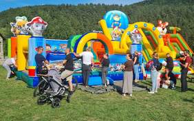 Pokaż zdjęcie: Na zdjęciu widoczne są duże dmuchane, kolorowe  konstrukcje na których bawią się dzieci, przy nich stoją dorośli