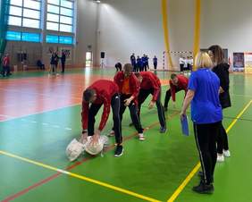 Pokaż zdjęcie: 4 mężczyzn uczestnicy w konkurencji sportowej. Są na hali sportowo-widowiskowej.