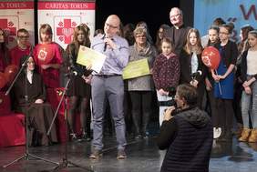 Brat osoby obdarowanej odbiera czek. Na drugim planie stoją ks. Daniel Adamowicz, wolontariusze Caritas oraz uczestnicy akcji