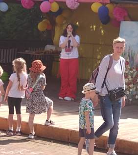 Pokaż zdjęcie: Na scenie jest nastoletnia wokalistka ubrana w czerwone lniane spodnie oraz koszulkę z nadrukiem na krótki rękaw. Ma rozpuszczone lekko kręcone czarne włosy do ramion. Na nosie filuterne okulary przeciwsłoneczne.  