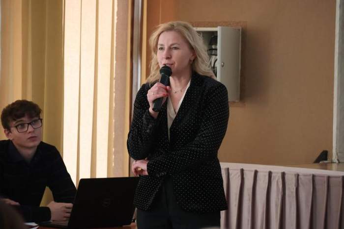 Pokaż zdjęcie: Zdjęcie kobiety, blondynki ubranej w czarną marynarkę, kobieta trzyma w ręku mikrofon.