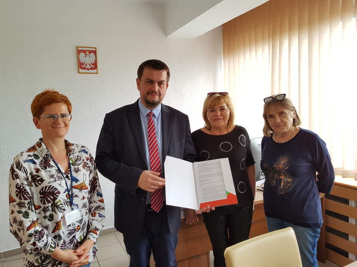 Pokaż zdjęcie: Dwie Panie ze Stowarzyszenia oraz Dyrektor Oddziału wraz z pracownicą Oddziału stoją obok siebie w Gabinecie Dyrektora a Dyrektor trzyma w ręku podpisaną umowę