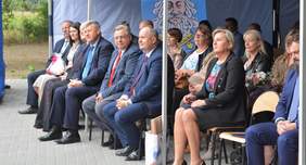 Pokaż zdjęcie: Grupa osób elegancko ubrana siedzi pod niebieskim namiotem