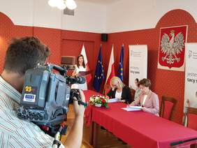 Pokaż zdjęcie: Dwie osoby siedzą przy stole konferencyjnym i podpisują dokumenty.