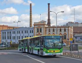 Pokaż zdjęcie: Autobus w kolorach zółto-biało-zielonym na rondzie na tle kamienic miasta