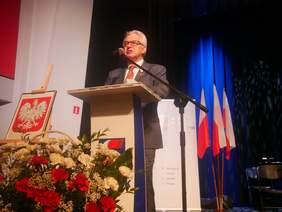 Pokaż zdjęcie: Mężczyzna stoi przy pulpicie i przemawia do słuchaczy