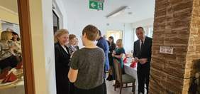 Pokaż zdjęcie: W sali osoby składają sobie życzenia, dzielą się opłatkiem.