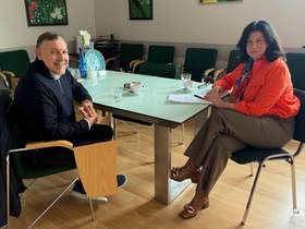 Sala konferencyjna. Przy szklanym stole siedzą kobieta i mężczyzna. Rozmawiają, na stole leżą dokumenty.