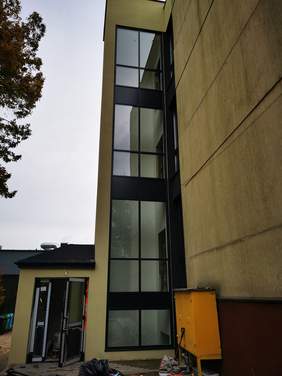 Pokaż zdjęcie: Szyb windy przy budynku ma częściowo szklane ściany. 