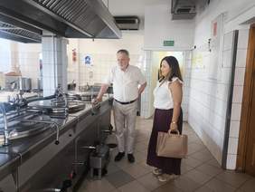 Pokaż zdjęcie: Dwie osoby zwiedzają zaplecze kuchenne ZAZ w Stoczku Łukowskim. W pomieszczeniu znajdują się profesjonalne urządzenia gastronomiczne.