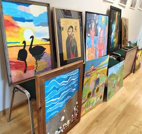 Pokaż zdjęcie: Prace zgłoszone w ramach konkursu "Sztuka osób niepełnosprawnych". Obrazy ułożone wzdłuż ściany w siedzibie Oddziału