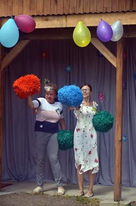 Pokaż zdjęcie: Na scenie stoją dwie kobiety i tańczą, w rękach trzymają kolorowe pompony