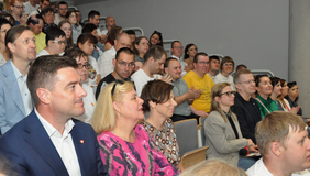 Pokaż zdjęcie: Grupa kilkudziesięciu osób siedzi na widowni w dużej sali. Możemy dostrzec, że część z tych osób bije brawa. Wiele osób jest uśmiechniętych.