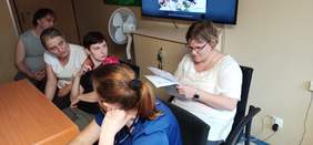 Pokaż zdjęcie: 1 chłopak i cztery dziewczyny siedzą obok siebie przy stole jedna z nich czyta pozostali słuchają