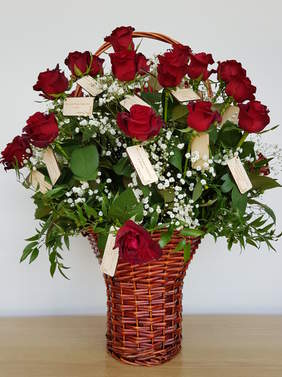 Brązowy kosz z czerwonymi rózami, do każdej dołączona jest mała, drewniana wizytówka
