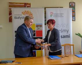 Prezydent Miasta Białegostoku Tadeusz Truskolaski oraz p.o. Dyrektora Oddziału Podlaskiego PFRON Grażyna Bogdańska przekazują sobie podpisane umowy.
