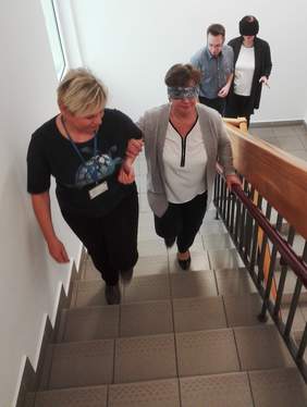 Pokaż zdjęcie: Cztery osoby idące po schodach, dwie mają zasłonięte oczy