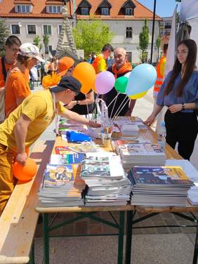 Pokaż zdjęcie: Stroisko infromacyjne Oddziału Małopolskiego PFRON - uczestnicy wydarzenia sięgają po materiały informacyjne znajdujące się na stoliku